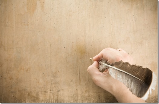 Hand holding quill pen preparing to write on blank parchment