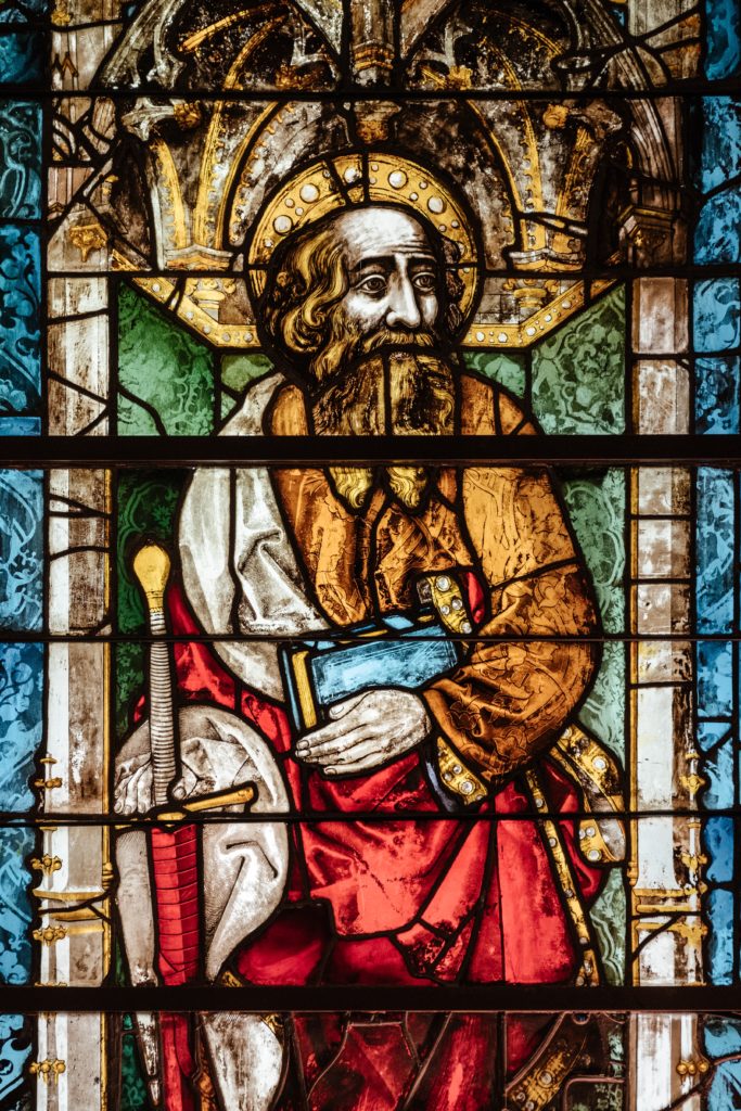 Stained glass image of saint holding a Bible and a sword